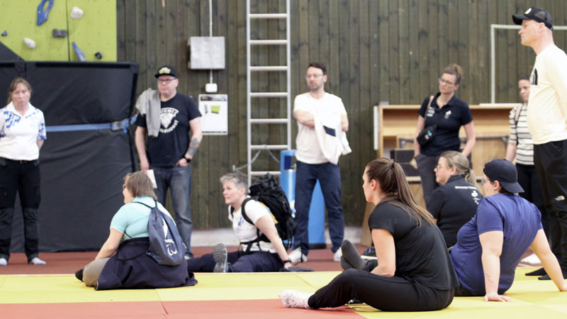 Henkilöitä istumassa ja seisomassa liikuntahallin lattialla kuunnellen koulutusta.