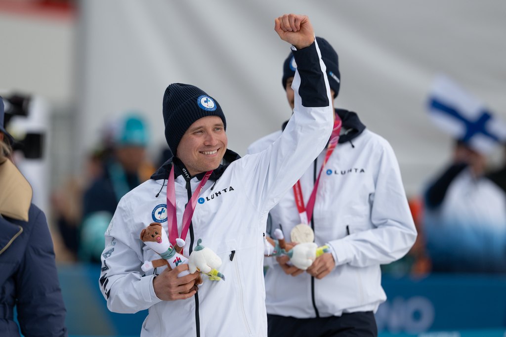 Inkki Inola tuulettamassa mitalienjakotilaisuudessa hopeamitali kaulassaan ja kisamaskotti kädessään. Taustalla opashiihtäjä Reetu Inkilä.