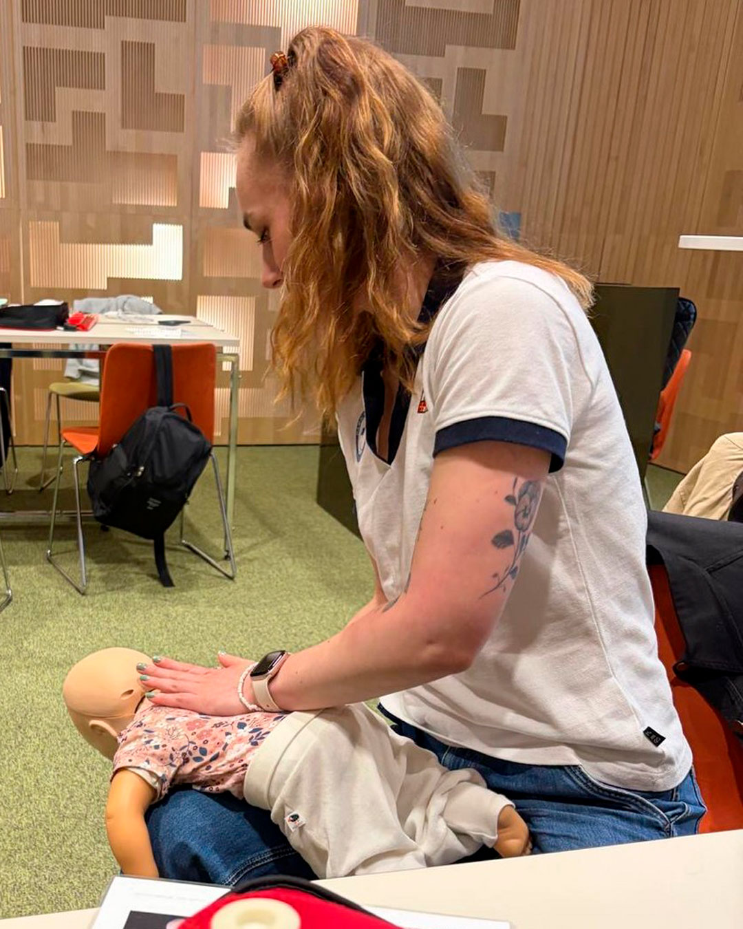 Henkilö pelastamassa vauvanukkea tukehtumiselta lyömällä kämmenellä lapaluiden väliin, nuken maatessa vatsallaan auttajan reidellä.