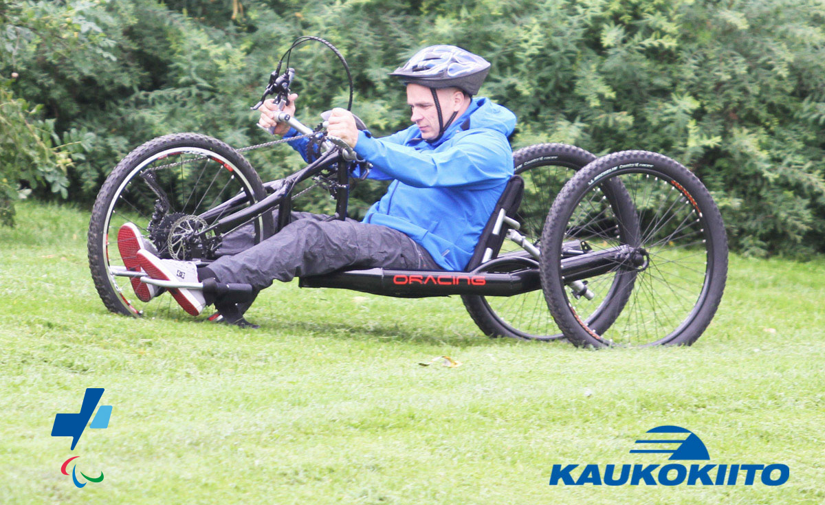 Käsipyöräilijä. Kuvan päällä Paralympiakomitean ja Kaukokiidon logot.